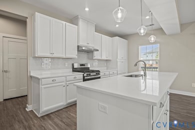 Kitchen featuring tasteful backsplash, stainless steel range with gas cooktop, hanging light fixtures, white cabinetry, and an island with sink