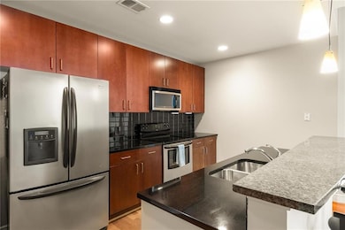 Kitchen featuring stainless steel appliances, a sink, dark countertops, a peninsula, and tasteful backsplash