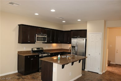 Kitchen with stainless steel appliances, recessed lighting, dark stone countertops, a breakfast bar, and a center island with sink