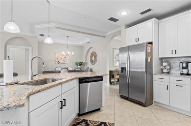 Kitchen featuring arched walkways, white cabinets, appliances with stainless steel finishes, light stone countertops, and a chandelier