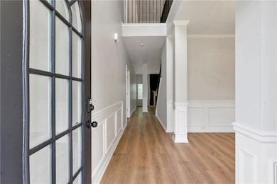 Entrance foyer with light wood-style flooring, ornate columns, a decorative wall, a wainscoted wall, and crown molding