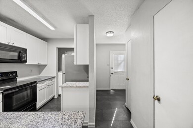 Kitchen featuring black appliances, white cabinets, a textured ceiling, and light stone countertops