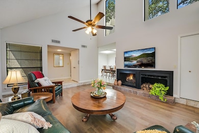 Living area featuring a warm lit fireplace, high vaulted ceiling, wood finished floors, and a ceiling fan