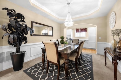 Dining space featuring a tray ceiling, a chandelier, wainscoting, ornamental molding, and arched walkways