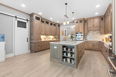 Kitchen with tasteful backsplash, light countertops, a barn door, a kitchen island, and light wood-type flooring