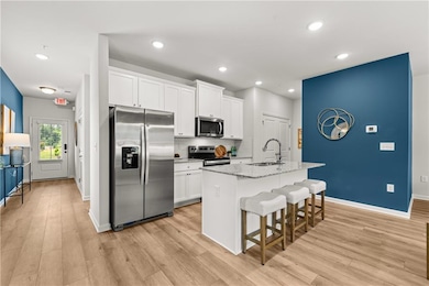 Kitchen featuring stainless steel appliances, a breakfast bar, light stone countertops, white cabinetry, and recessed lighting