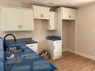 Kitchen with white cabinets, light wood-type flooring, and dark stone countertops