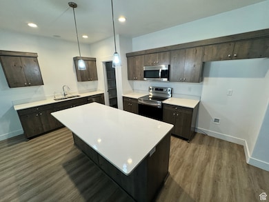 Kitchen with stainless steel appliances, dark brown cabinets, light countertops, a center island, and wood finished floors
