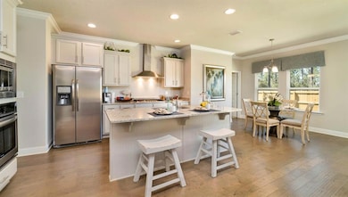 Kitchen featuring crown molding, appliances with stainless steel finishes, wall chimney exhaust hood, light stone counters, and a kitchen bar