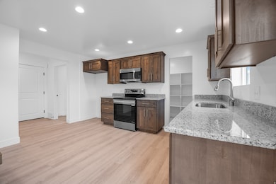 Kitchen with appliances with stainless steel finishes, light stone counters, light wood-style floors, recessed lighting, and dark brown cabinetry