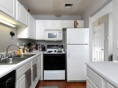 Kitchen featuring white appliances, light countertops, white cabinetry, a textured ceiling, and dark wood-style flooring
