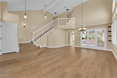 Unfurnished living room featuring high vaulted ceiling, stairway, light wood-style floors, beamed ceiling, and a chandelier