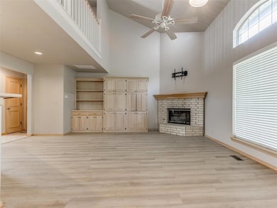 Unfurnished living room with a high ceiling, baseboards, a ceiling fan, a fireplace, and light wood finished floors
