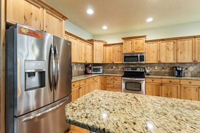 Kitchen with stainless steel appliances, light brown cabinets, recessed lighting, backsplash, and light stone countertops