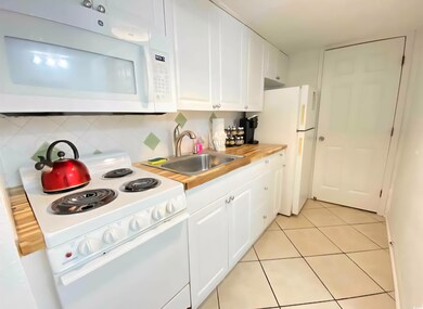 Kitchen featuring white appliances, a sink, white cabinetry, light countertops, and light tile patterned floors