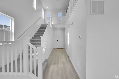 Entryway featuring healthy amount of natural light, light wood-type flooring, a towering ceiling, stairway, and recessed lighting