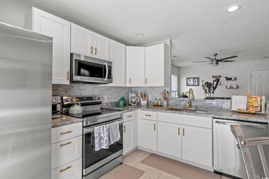 Kitchen featuring stone counters, sink, white cabinets, light tile patterned floors, and stainless steel appliances