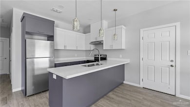 Kitchen featuring white cabinets, stainless steel appliances, a peninsula, hanging light fixtures, and wood tiled floors