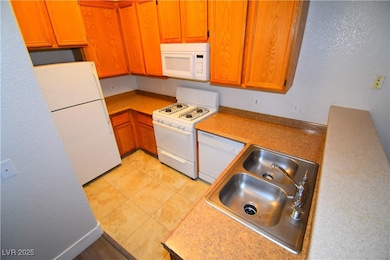 Kitchen with white appliances, light countertops, a textured wall, brown cabinets, and light tile patterned floors