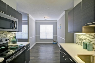 Kitchen with appliances with stainless steel finishes, tasteful backsplash, a textured ceiling, dark hardwood / wood-style flooring, and ornamental molding