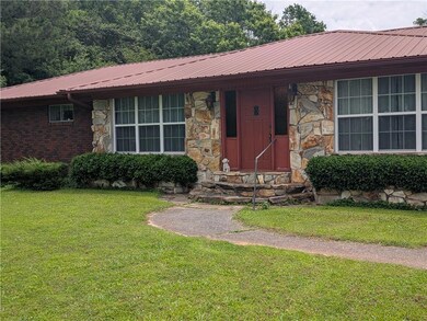 Ranch-style home with stone siding, a front yard, metal roof, and entry steps