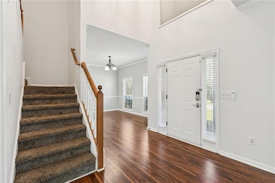 Foyer featuring crown molding, a towering ceiling, a chandelier, dark wood finished floors, and stairs