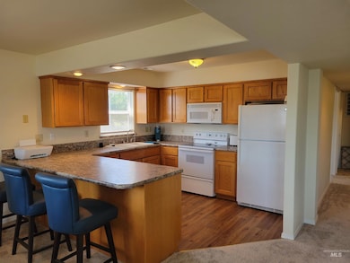 Kitchen featuring white appliances, a peninsula, brown cabinetry, and a breakfast bar area
