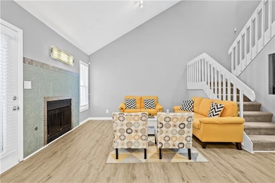 Sitting room with wood finished floors, stairs, a tiled fireplace, high vaulted ceiling, and baseboards