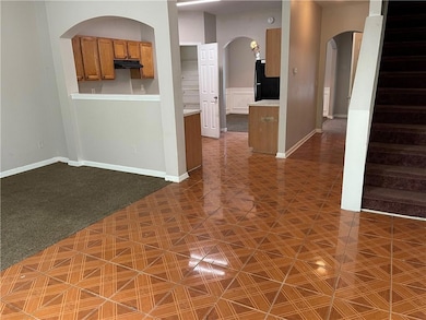 Kitchen featuring brown cabinetry, arched walkways, freestanding refrigerator, light countertops, and dark carpet