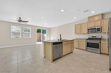 Kitchen with stainless steel appliances, light brown cabinetry, light stone countertops, open floor plan, and a kitchen island with sink
