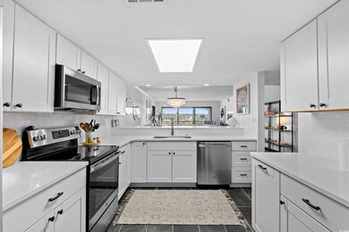 Kitchen with tasteful backsplash, stainless steel appliances, white cabinetry, light stone counters, and dark tile patterned flooring
