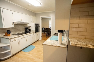 Kitchen with black appliances, light wood-style flooring, under cabinet range hood, crown molding, and tasteful backsplash