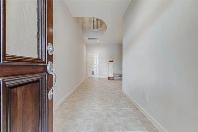 Step inside to a bright and open tiled foyer that instantly feels expansive thanks to a soaring two-story ceiling and curved architectural cutout above. This space introduces the home’s graceful flow and neutral palette. A carpeted staircase with wood rail accents curves up to the main living areas, inviting exploration of the home’s elegant, functional layout.