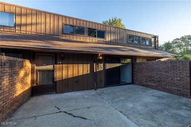 View of front facade featuring a patio, a shingled roof, brick siding, and board and batten siding