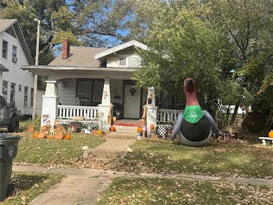 Bungalow-style home featuring a porch, a chimney, a front yard, and a shingled roof