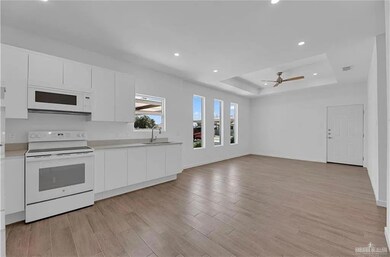 Kitchen with white appliances, a tray ceiling, white cabinetry, light wood-style floors, and recessed lighting