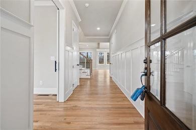 Corridor with light wood-type flooring, a decorative wall, stairs, ornamental molding, and recessed lighting