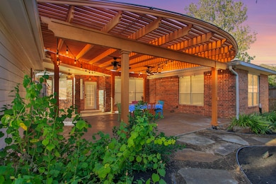 Beautiful covered patio with custom pergola, string lights, and ceiling fans—perfect for outdoor dining and entertaining. Stamped-concrete flooring and lush landscaping create a relaxing backyard retreat.