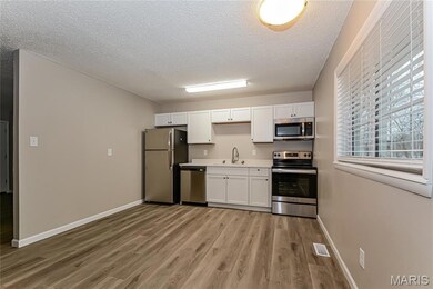 Kitchen featuring appliances with stainless steel finishes, white cabinets, a textured ceiling, light countertops, and light wood-style flooring