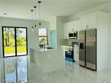 Kitchen featuring appliances with stainless steel finishes, white cabinetry, light marble finish flooring, hanging light fixtures, and recessed lighting