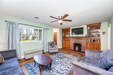 Living room with a brick fireplace, dark wood-type flooring, built in features, and ceiling fan