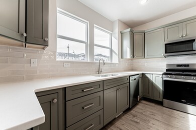 Kitchen featuring gray cabinetry, appliances with stainless steel finishes, decorative backsplash, light wood-style flooring, and light stone counters