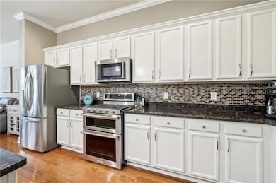 Kitchen featuring appliances with stainless steel finishes, ornamental molding, white cabinetry, decorative backsplash, and dark stone counters