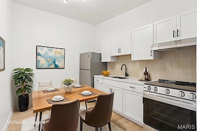 Kitchen featuring stainless steel appliances, white cabinets, under cabinet range hood, light wood-style flooring, and tasteful backsplash