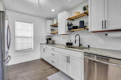Kitchen with open shelves, a textured ceiling, stainless steel appliances, wood finished floors, and light stone counters
