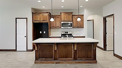 Kitchen featuring appliances with stainless steel finishes, arched walkways, recessed lighting, light countertops, and baseboards