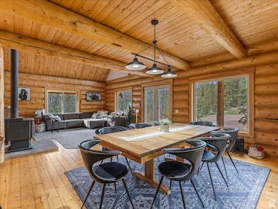 Dining room with a wood stove, light wood-type flooring, a wood ceiling with exposed beams, and rustic walls