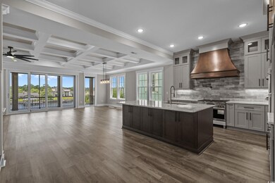 Kitchen featuring high end stainless steel range, premium range hood, open floor plan, ceiling fan, and coffered ceiling