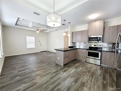 Kitchen featuring appliances with stainless steel finishes, a peninsula, dark countertops, open floor plan, and backsplash