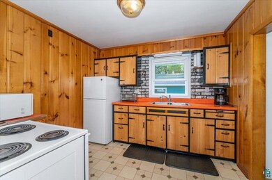 Kitchen featuring a sink, white appliances, wood walls, brown cabinets, and ornamental molding